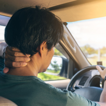 Man sitting in car in discomfort holding neck