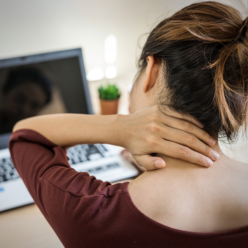 Woman in front of laptop holding neck