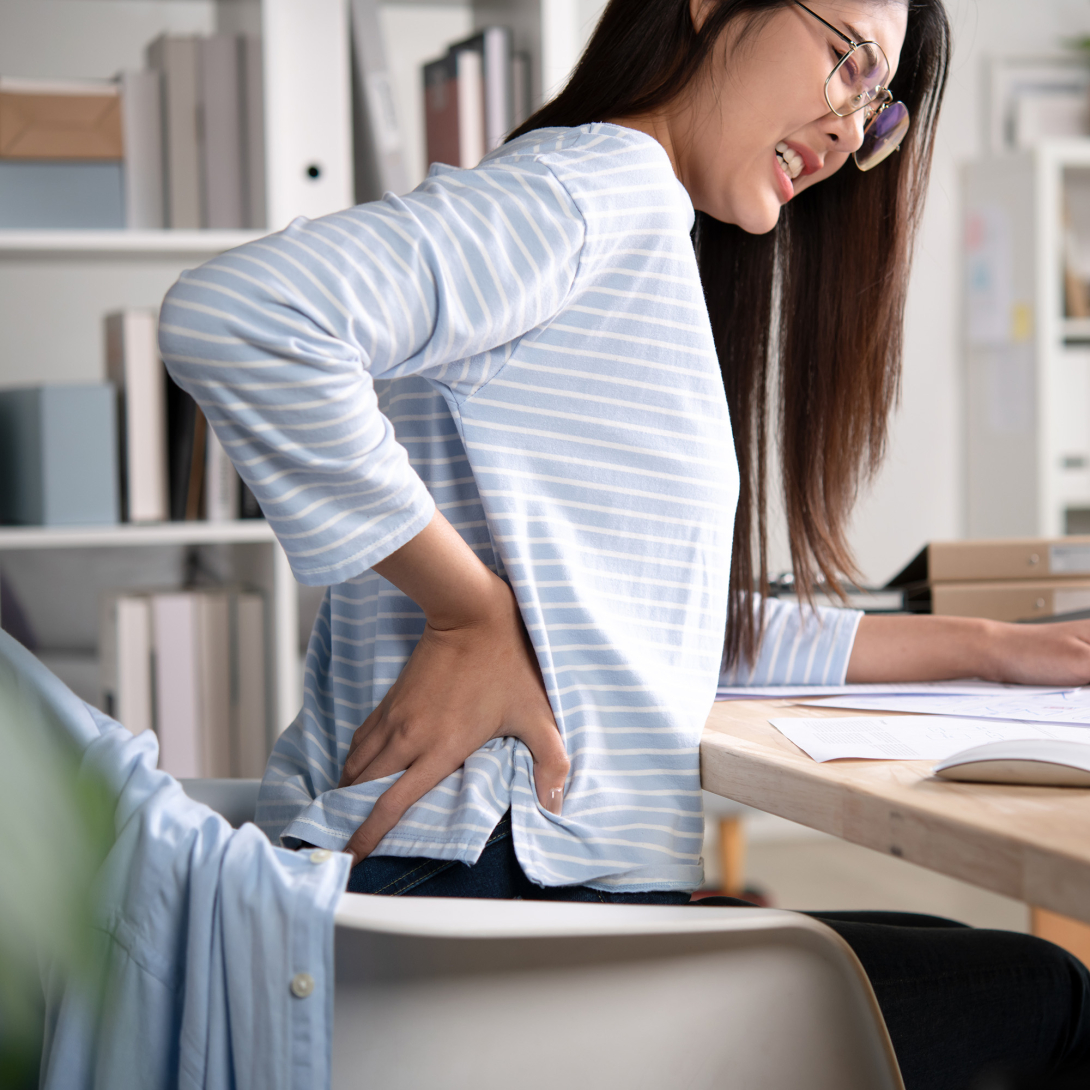 Asian woman holding lower back while working at desk