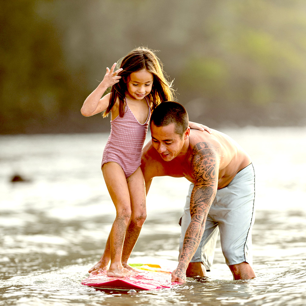Man teaching his preschool aged daughter how to surf in Honolulu